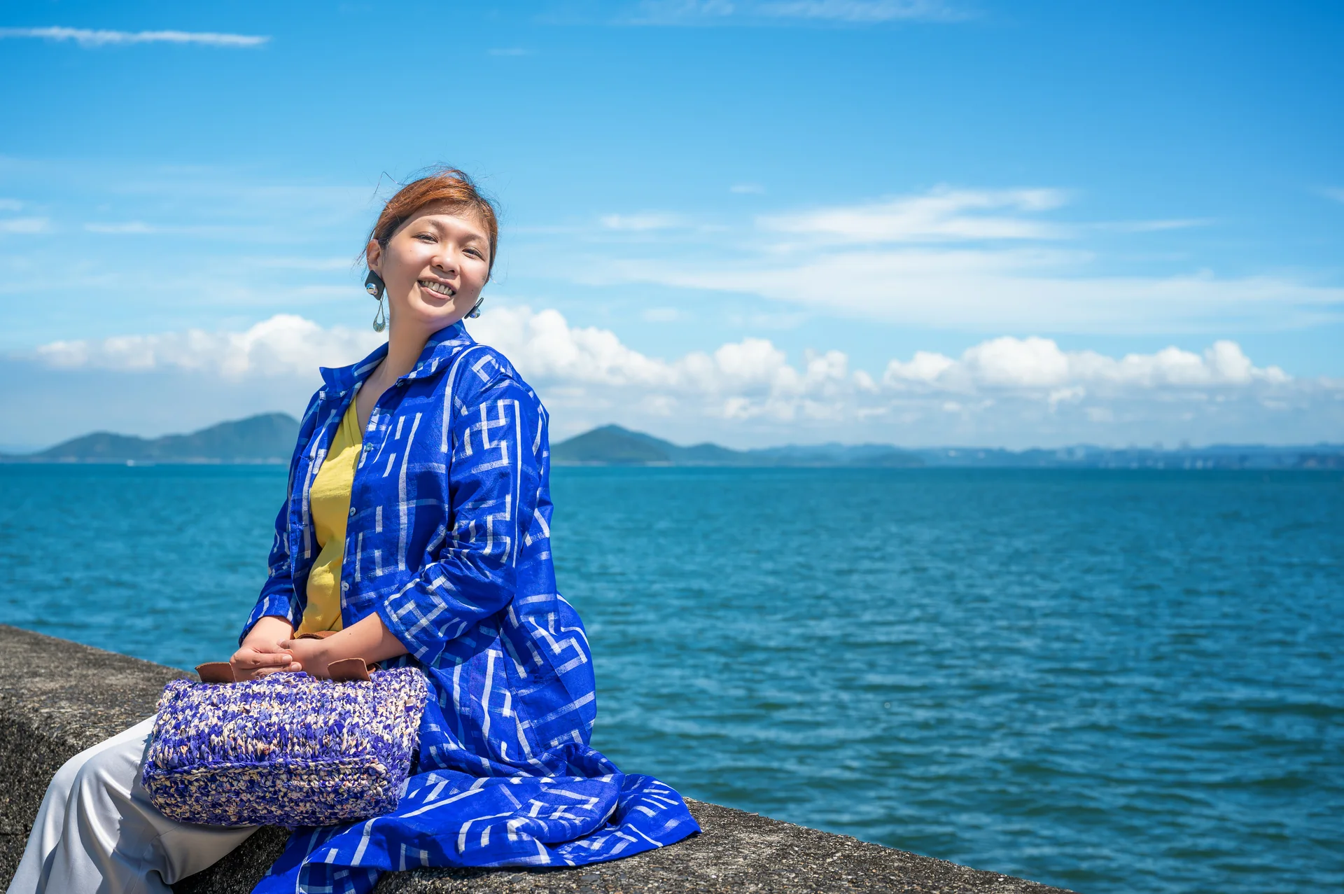 青い着物服をまとい、海辺で微笑む女性